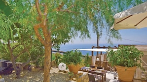 Eine Terrasse im Freien mit Tisch und Stühlen, umgeben von Kübelpflanzen und Blick aufs Meer.