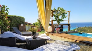 Ein Poolbereich mit Liegestühlen, einer Holzterrasse und Blick auf das Meer.