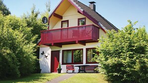 Una casa a due piani con un balcone rosso, un piccolo giardino e un vialetto che conduce a una panchina.