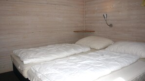 Una camera piccola con un letto singolo, pareti in legno e un semplice portalampada in metallo.