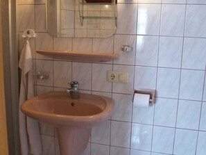 Un baño con lavamanos, espejo, toallero y repisa.