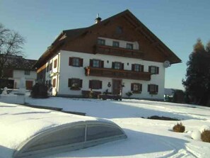 Ein zweistöckiges Gebäude mit geneigtem Dach und einem Balkon im oberen Stockwerk, der Boden ist mit Schnee bedeckt.