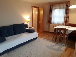 Una habitación con un sofá, una mesa de comedor con sillas, una lámpara y un ventanal con cortinas.