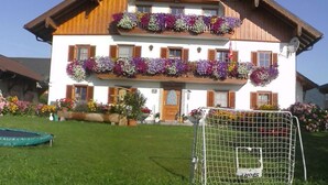 A two-story building with balconies, a front door, and a small garden area. - Apartment 1 - Ferienhof Nussbaumer (Gaisberg)