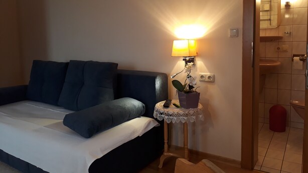 Ein Schlafzimmer mit einem Bett, einem Nachttisch mit Lampe, einer Topfpflanze und einem durch eine offene Tür einsehbaren Badezimmer.