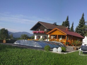 Ein Haus mit einem geschwungenen Glasanbau, einer Holzterrasse und einem Blick auf die Berge.