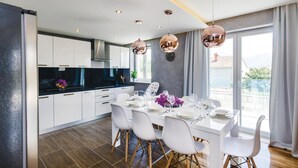 Een moderne keuken met witte kasten, een zwart aanrecht en een eethoek voor zes personen, compleet met witte stoelen en een tafel.