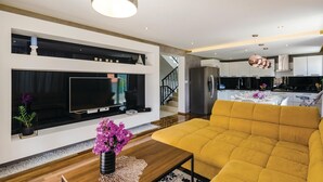 Een moderne woonkamer met een grote flatscreen-tv, een gele bank en een houten salontafel.