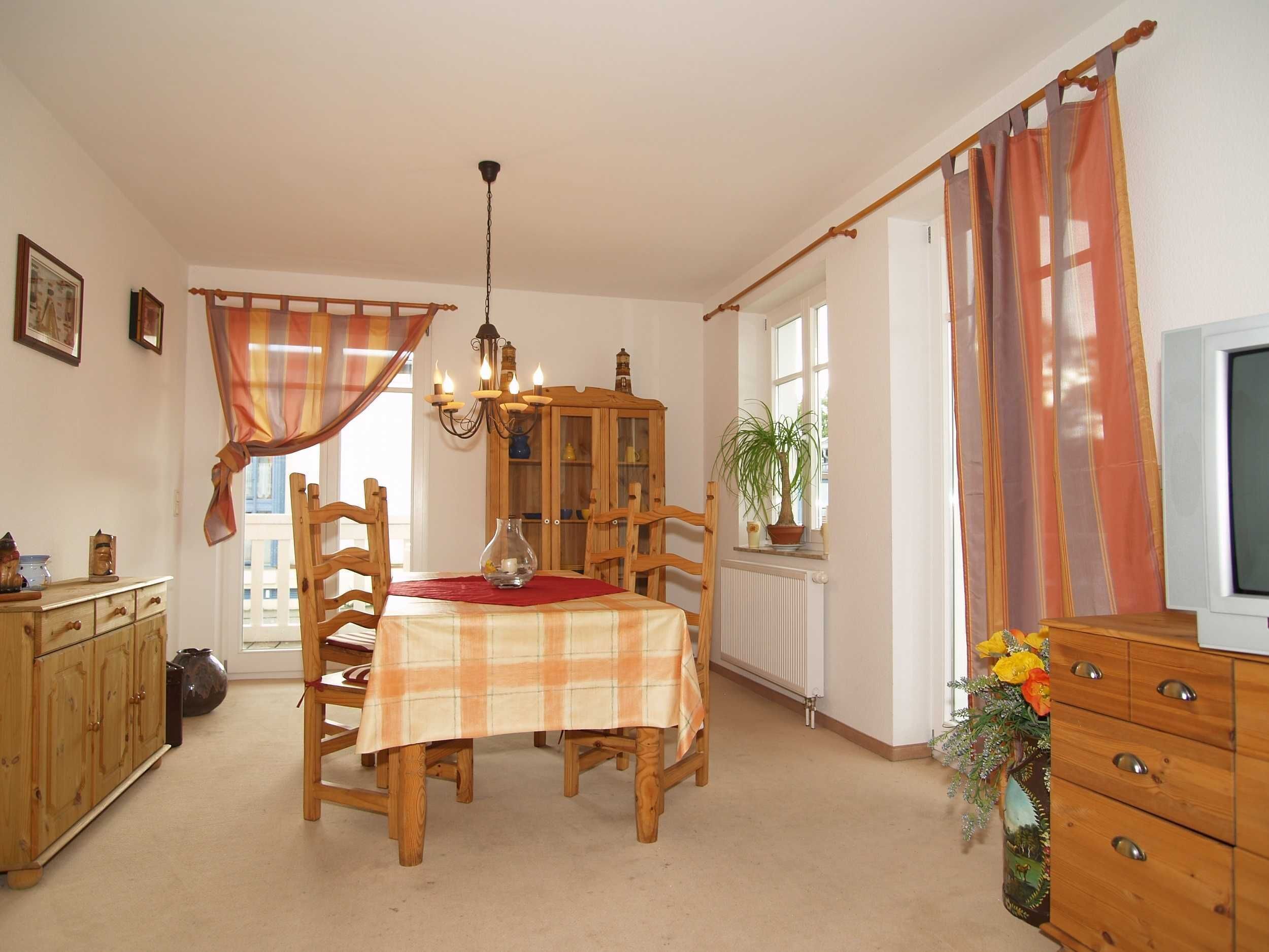 A dining area with a wooden table, chairs, a chandelier, and a cabinet.