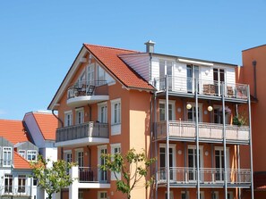 A multi-story building with balconies, large windows, and a red-tiled roof.