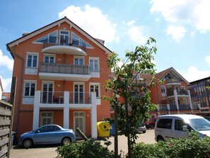 Een meerlaags woongebouw met balkons, een auto ervoor en een boom op de voorgrond.