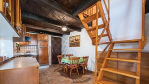 Une cuisine rustique avec des meubles en bois, un sol carrelé, un coin repas avec des chaises et une échelle en bois.