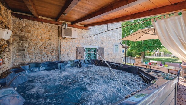Un espace extérieur doté d’un jacuzzi en pierre, avec un plafond en bois et un ventilateur de plafond.