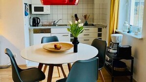 Una cocina moderna con una mesa blanca, sillas azul verdosas y una lámpara colgante roja.