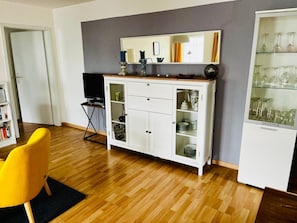 En moderne stue med et hvidt skab, en gul stol og et glasvitrineskab med vinglas.