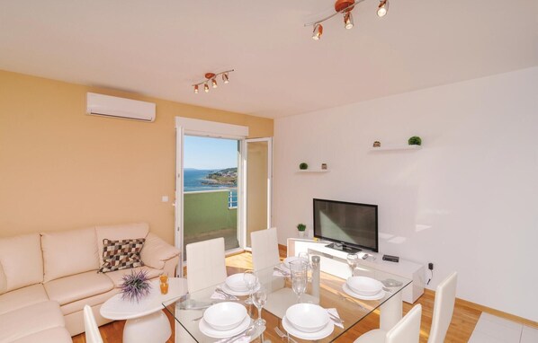 Un salon moderne avec une table à manger en verre pour quatre personnes, un canapé, un téléviseur à écran plat et un balcon offrant une vue sur la mer.