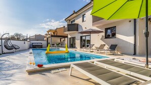 A swimming pool with lounge chairs and a bright green umbrella. - Lovely home in Pula with sauna (Pula)