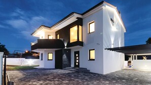 A modern two-story house with a balcony, a driveway, and a well-lit entrance. - Lovely home in Pula with sauna (Pula)