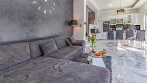 A modern living room with a grey sofa, a glass coffee table with flowers, and a kitchen in the background. - Lovely home in Pula with sauna (Pula)