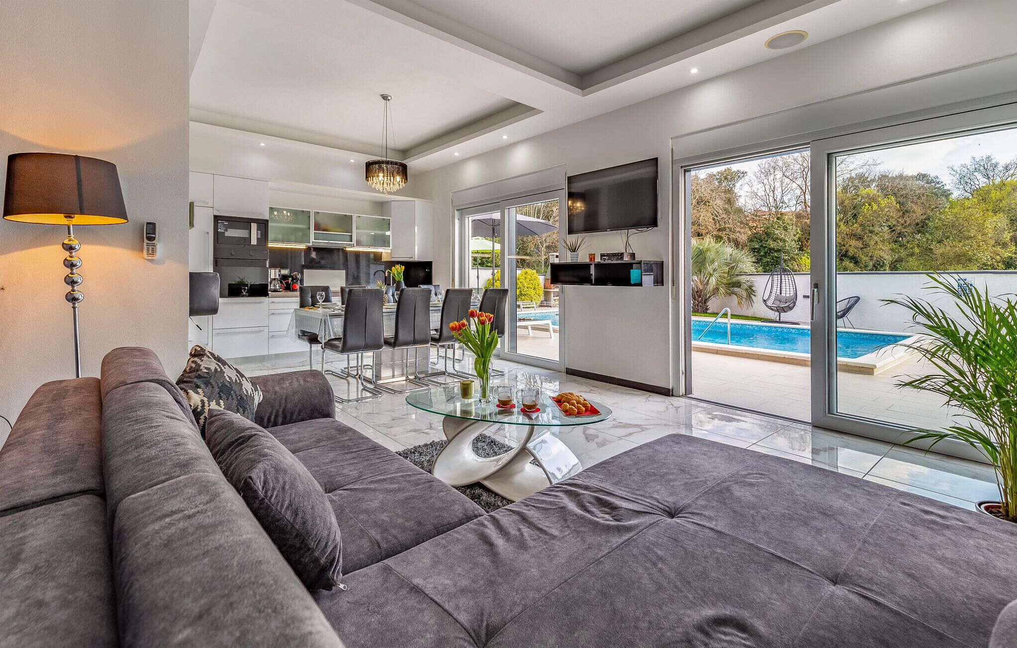 A modern living room with a sofa, a glass coffee table, and a view of a swimming pool.
