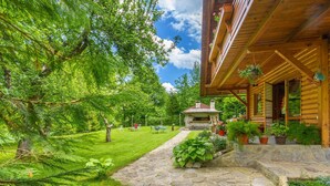 Una baita di legno con un vialetto in pietra che conduce a un camino in pietra, immersa nel verde e sotto un cielo sereno.