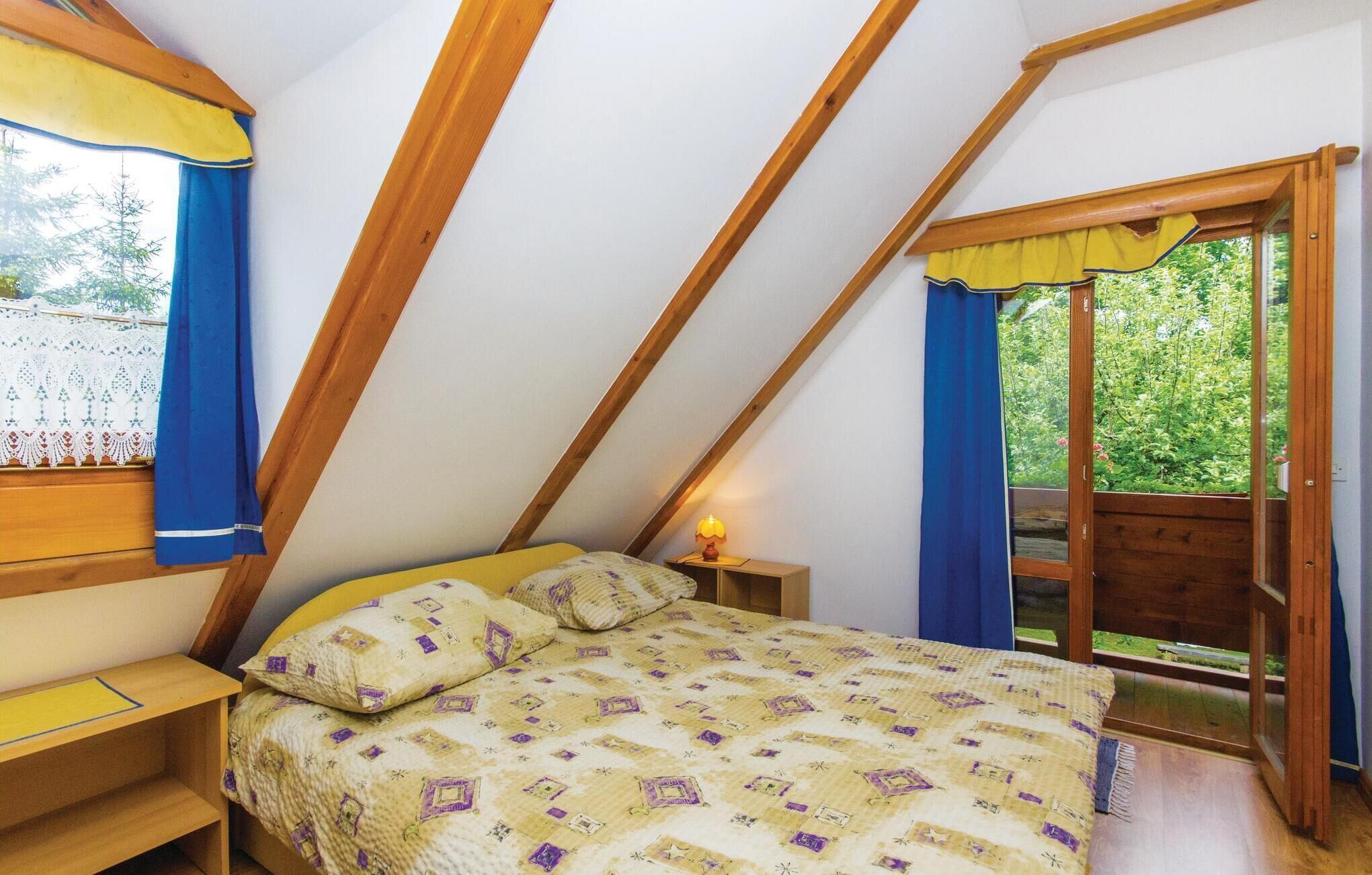 Une chambre avec un plafond en pente, un lit avec une literie à motifs, une table de chevet avec une lampe et une fenêtre avec des rideaux.