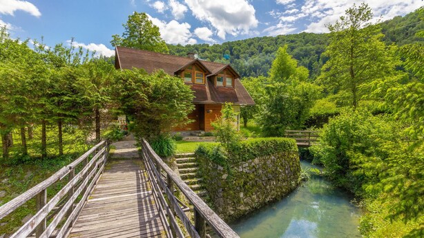 Una baita di legno con fondamenta in pietra, immersa nel verde e bagnata da un ruscello cristallino.