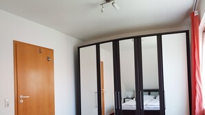 A bedroom with a wooden door, a wardrobe with mirrors, a bed, and a red carpet. - Apartment 03.12 - House 12 (Trassenheide)