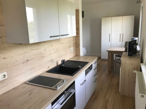 A modern kitchen with white cabinets, a wooden countertop, a built-in oven, and a dining area with a table and chairs.
