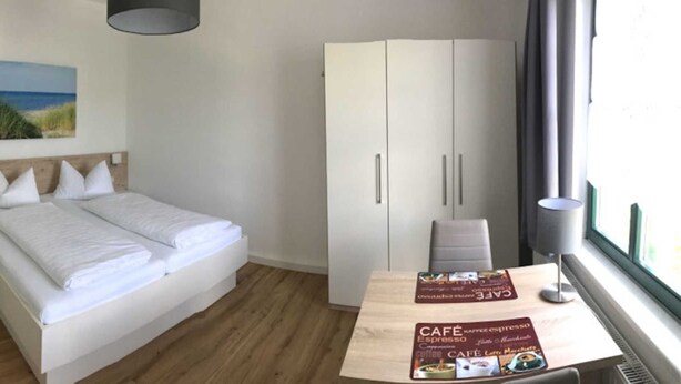 Ein Hotelzimmer mit Bett, Kleiderschrank, Schreibtisch und Speisekarte sowie einem Fenster.