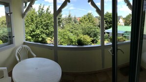 Ein Zimmer mit einem runden Tisch und einem weißen Stuhl, einer Glastür, die nach draußen führt, und Blick auf Bäume und Gebäude.