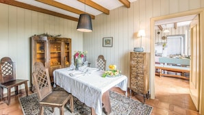 Une salle à manger avec une table en bois dressée pour quatre personnes, un buffet aux portes vitrées et une vue sur la cuisine.