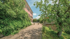 Un sentier pavé de pierres menant à un bâtiment à la façade rose et aux volets verts.