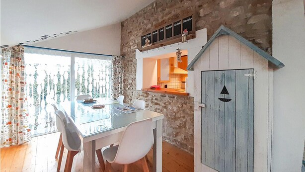 A cozy kitchen with a stone wall, a wooden table, and a door with a triangular cutout. - Amazing home in Ambleteuse with WiFi (Ambleteuse)