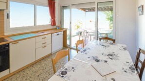 Una cocina con comedor, una ventana con cortinas, lavavajillas y una mesa con sillas.