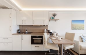 A modern kitchen with white cabinets, a wooden countertop, and a dining area with a table set for two. - Amazing apartment in Binz with house sea view (Prora/Rügen)