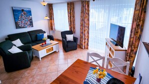 Un salon avec un canapé, un fauteuil, une table basse, un téléviseur et un tableau accroché au mur.