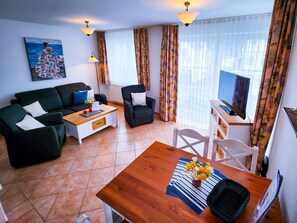 Un salon avec un canapé, un fauteuil, une table basse, un téléviseur et un tableau accroché au mur.