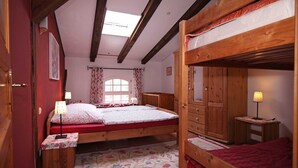 Une chambre avec un lit superposé, une armoire en bois, une table de chevet avec une lampe et un tapis à motifs floraux.