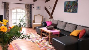 Un salon comprenant un canapé, un fauteuil, une table avec un panier, un vase de fleurs et un tapis coloré.