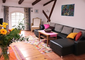 Un salón con un sofá, una silla, una mesa con una cesta, un jarrón con flores y una alfombra colorida.