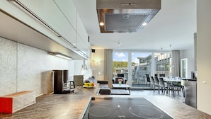 A modern kitchen with a built-in stove, a coffee machine, and a dining area with a table and chairs.
