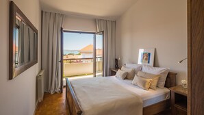 Ein Schlafzimmer mit Bett, Nachttisch, Lampe und Blick ins Freie.