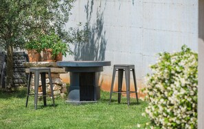 Relax in a serene outdoor space with a stone table and two stools, surrounded by lush greenery and a natural backdrop.