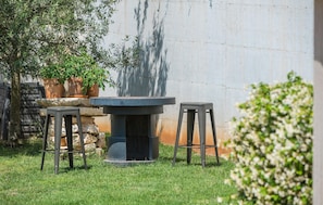 Relax in a serene outdoor space with a stone table and two stools, surrounded by lush greenery and a natural backdrop.