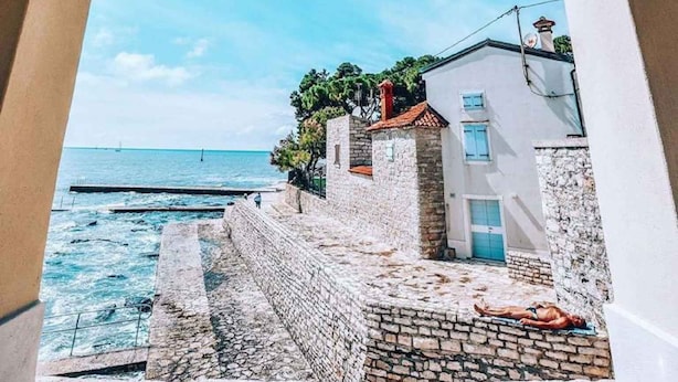 Vista costera a través de un arco, que conduce a un muro de piedra y un edificio con una puerta azul.