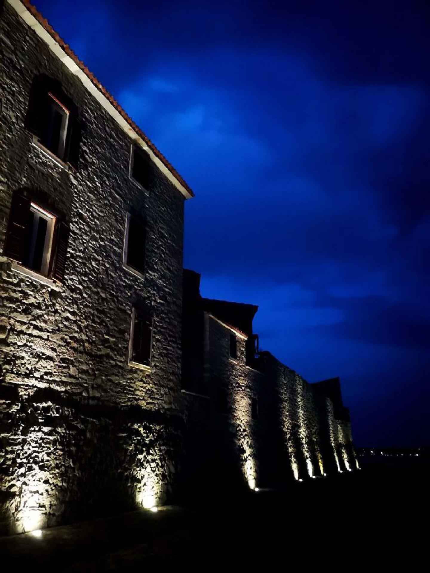 Un bâtiment en pierre doté de nombreuses fenêtres et d’un toit recouvert de tuiles rouges, éclairé par un système d’éclairage extérieur.