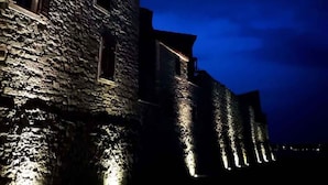 Un edificio de piedra con varias ventanas y techo de tejas rojas, iluminado por luces exteriores.