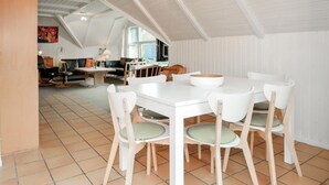 A dining area with a white table and chairs, a large window, and a kitchen in the background. - Stunning home in Blåvand with sauna (Blåvand)