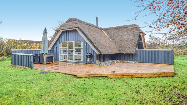 A thatched-roof house with a wooden deck and a large window. - Stunning home in Blåvand with sauna (Blåvand)